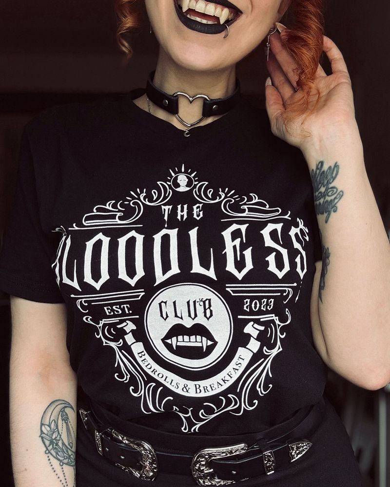 Picture of me in a black t-shirt with a white print. The print says "The Bloodless Club – Est. 2023 – Bedrolls & Breakfast". It’s a selfmade fanshirt for the game Baldur's Gate 3.