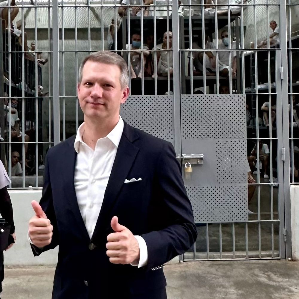 some inhuman fascist scum not worth mentioning doing the thumbs up gesture in front of an over crowded prison cell in CECOT, the El Salvadorian mega prison where the US traffics innocent humans