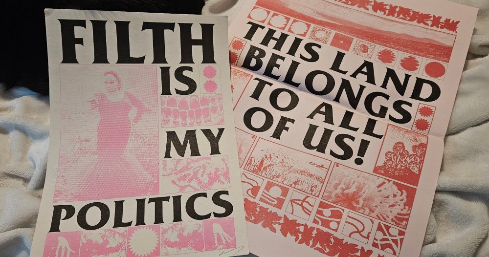 A photo of two posters, one pink and black A4 poster, and a red and black A3 poster. The A4 on reads in bold letters "Filth is my politics" with a pink picture of Divine from the John Waters movie Pink Flamingos, in the last Scene of the movie. Divine is wearing an extravagant dress in a close-body shape which fans out at the bottom. Between the text are a various panels with many different patterns and visual textures reminiscent of teeth and unidentifiable "filthy" things. The other poster reads "this land belongs to all of us" in bold black letters. The text is encased in many other panels with varying patterns and visual textures reminiscent of nature and scenic views.
