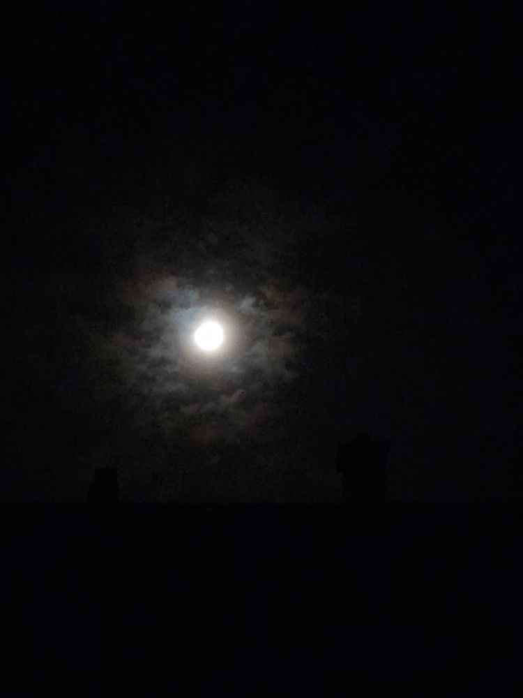 Full moon above a roof, a few clouds sorround it.
