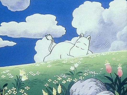 Moomin from the 90s Moomin Series laying in a field. The sky is lightly cloudy and deep blue. The field is full of green grass and flowers.