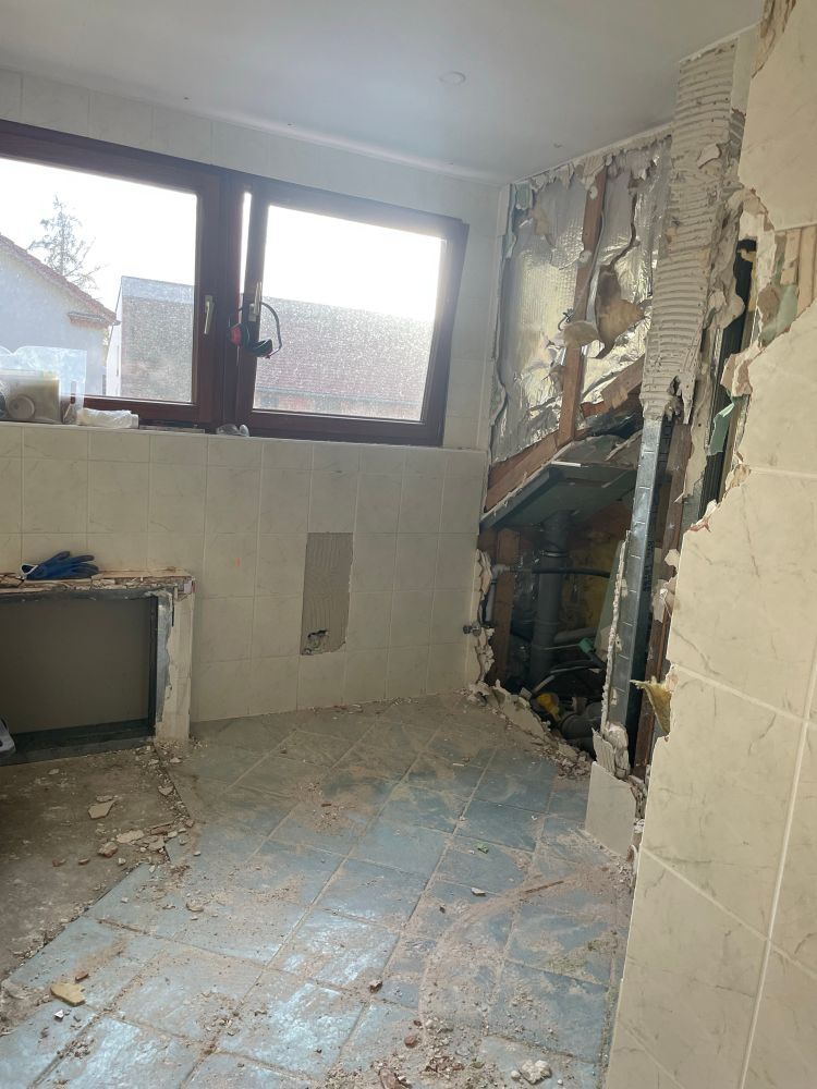 Bidet, Klo und Dusche sind weg, die Wand dahinter ist eingerissen. Staub und Schutt auf den Bodenfliesen. Im Hintergrund Fenster.