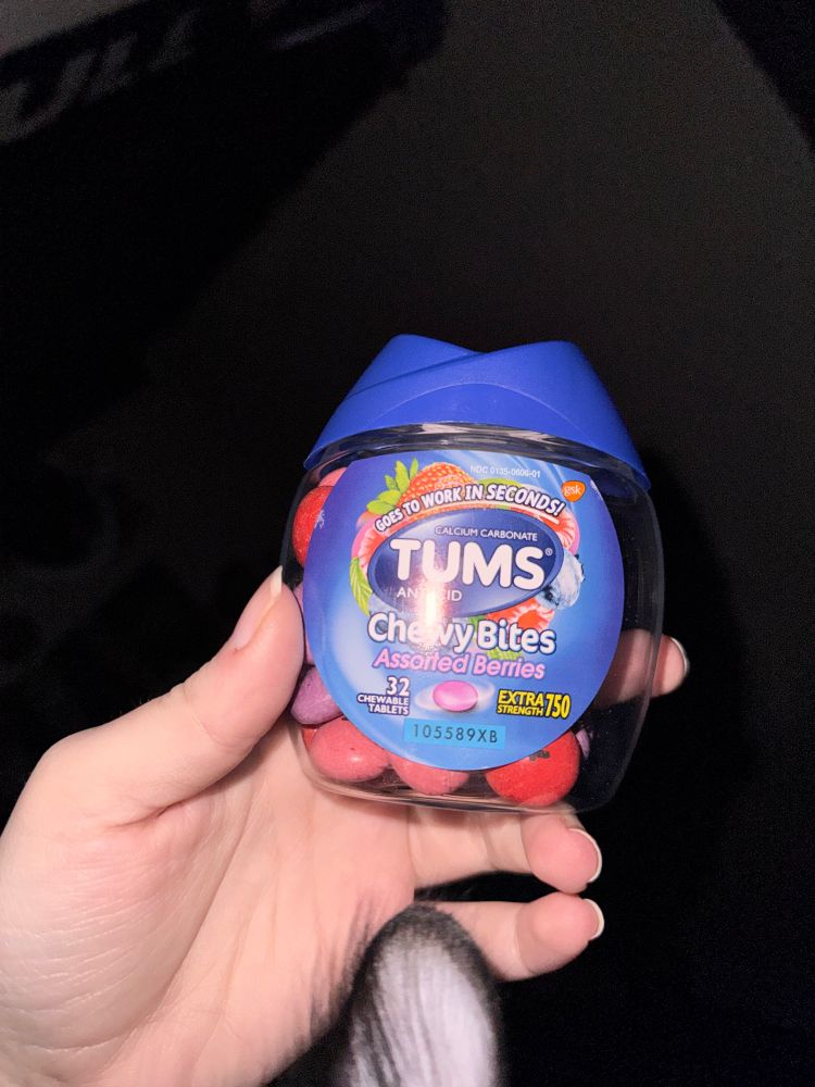 a container of Tums with a cats ear peaking into the bottom of the picture