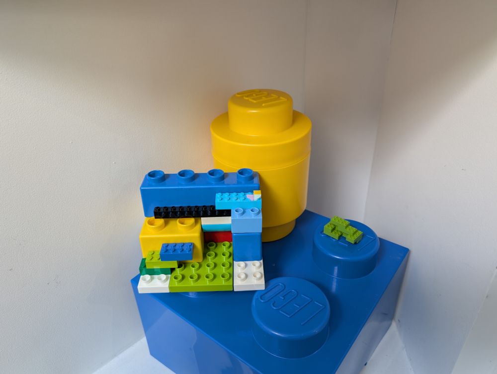 A large blue 2x2 block as a diamond with yellow cylinder block on rear stud.
On the right stud is a small green Lego structure constructed out of 2x4 bricks. The bricks are smaller than normal Lego bricks.
The left stud is a larger Lego structure, made out of 3 different sizes of brick. 