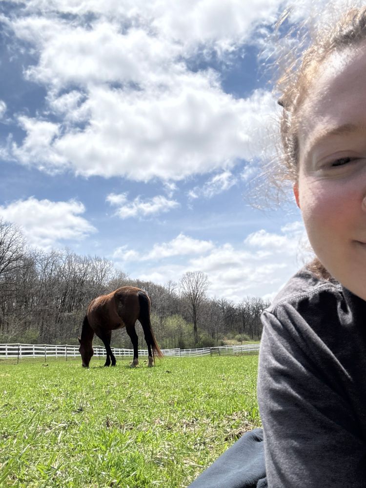 photo of me lying down and just the side of my face is visible with a bat horse grazing in the background 