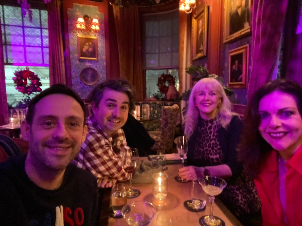 Four friends sit around a table in a dimly lit bar, each enjoying a cocktail 