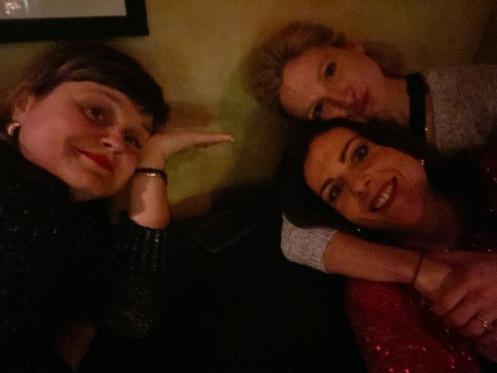 Three ladies are crowded around a table, the light is dim, it’s late.