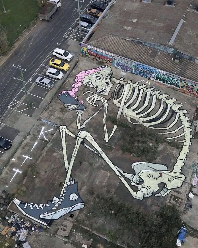 Mural in a parking lot of a skull playing with a phone while its brains are leaking out 