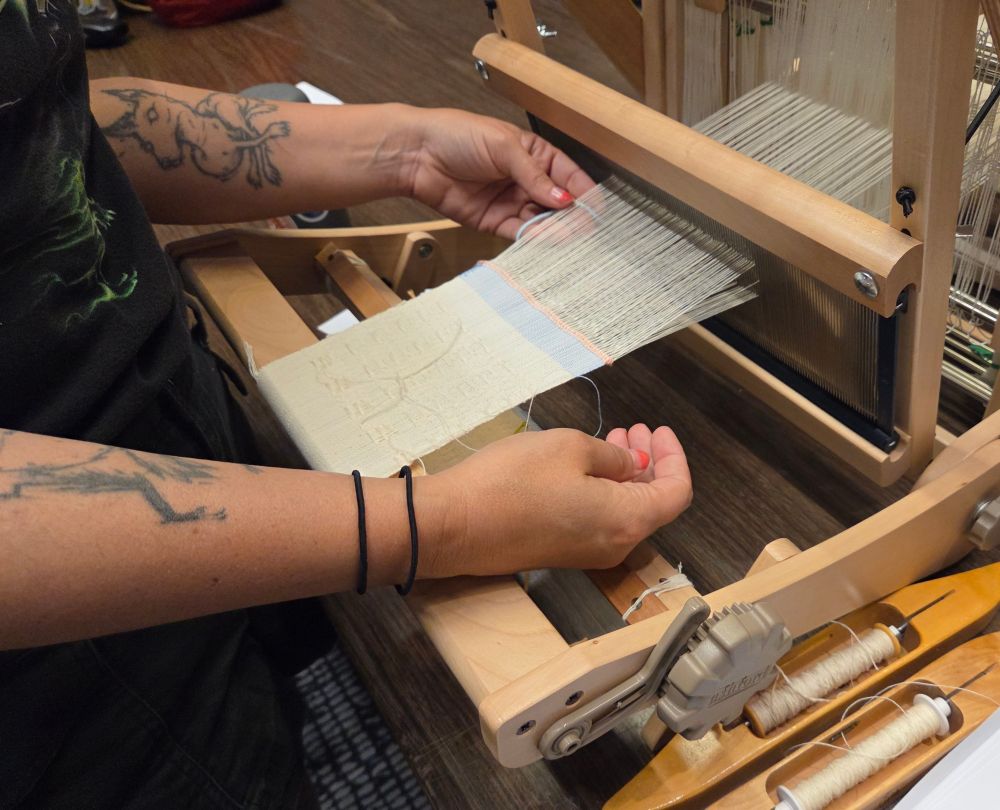 Hands weaving a cream colored sample at a loom