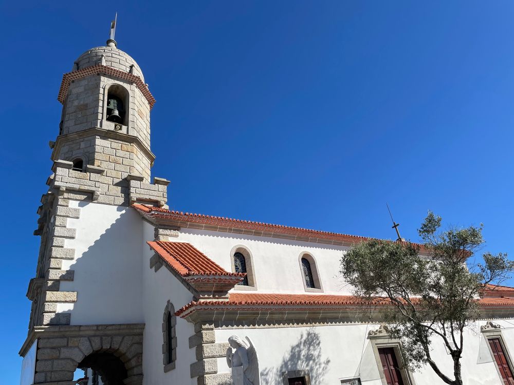 A white church with red tiled toof against a blue sky. A bell tower at the front with a domed roof. 