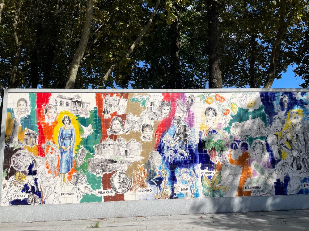 A colorful mural on a tiled wall, looks like watercolor marker on tile. Faces and scenes that are presumably significant locally. 
