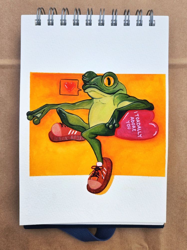 A frog sits and flirts with you, he wears a pair of red gym shoes and hangs over a candy heart that says - I TOADALLY ADORE YOU. 