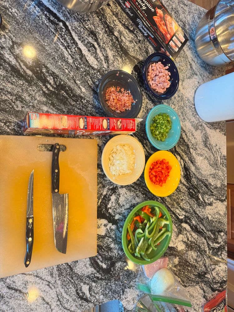 Kitchen counter with knives, cutting board, and bowls of ham, bacon, and veggies