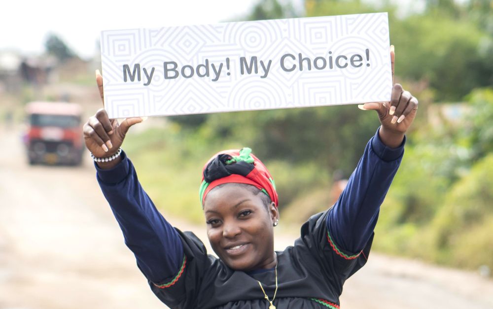 A young woman holds a sign which reads My Body My Choice.