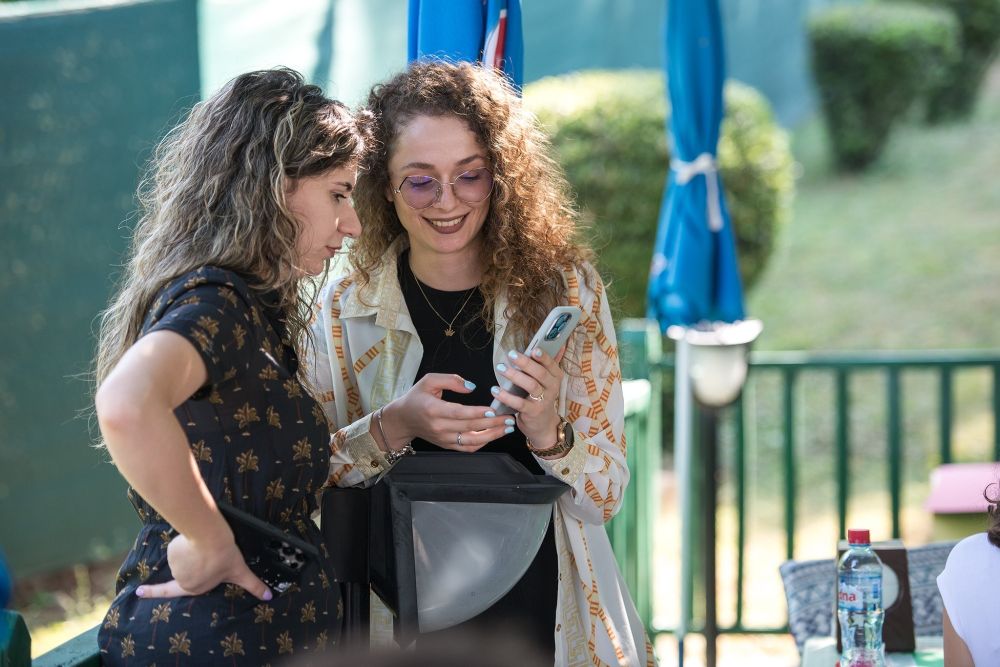 Two people with long curly hair look at a phone together