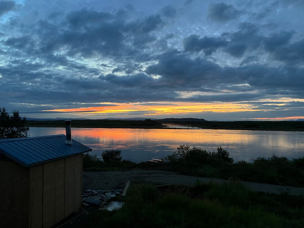 Orange band breaking thru a skate color sky over a wide river 