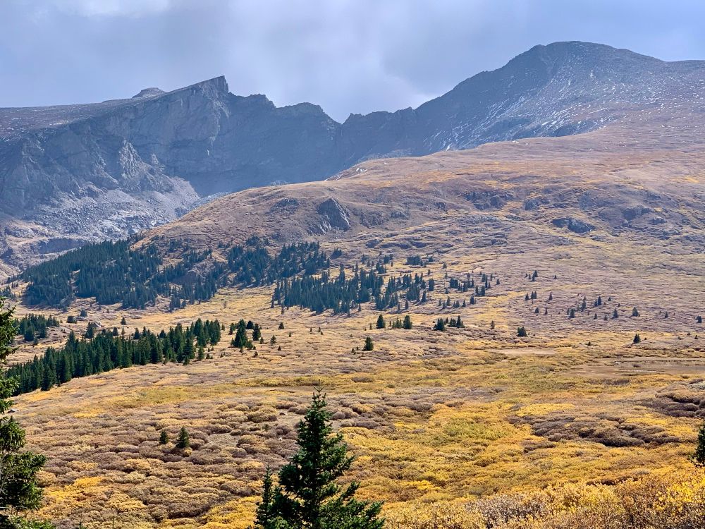 Snow speckled rocky mountain with jagged ridge line to the left of it 