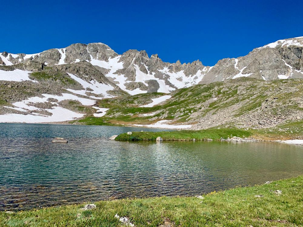 Snow splotched Rocky Mountains above an alpine tarn 