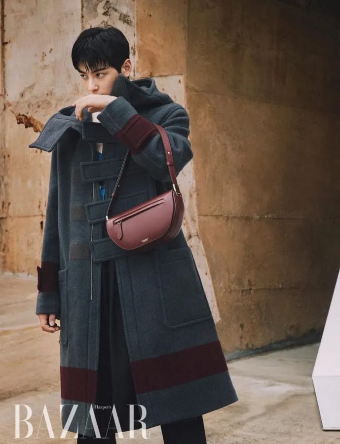 Cha Eunwoo is wearing a gray and burgundy coat with a matching burgundy bag