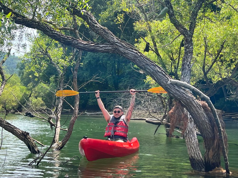Photo of my husband while kayaking on the lake. He has his paddle raised above his head like Doodle Bob holds his pencil. 
