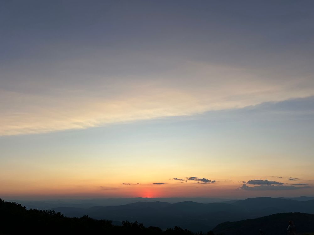 A sunset photo. The sun has just completely set over the mountains, leaving a small red glow above the very top of the mountains. 