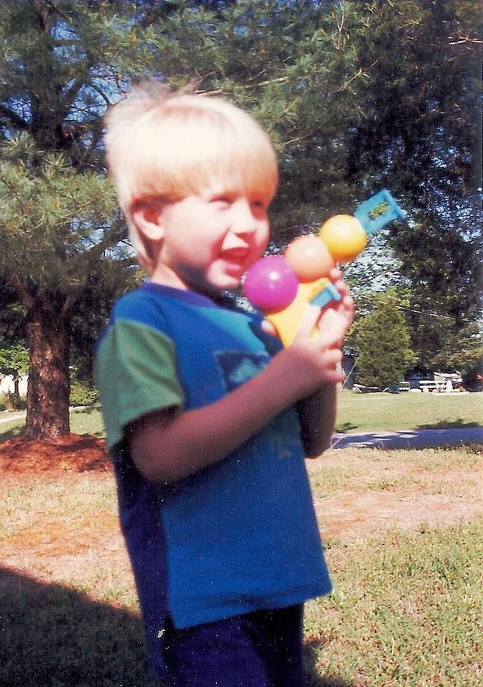 Childhood photo of me. I had platinum blonde, long  hair. I’m probably about 4-5 years old. I’m grinning while holding a bubble blowing gun. 