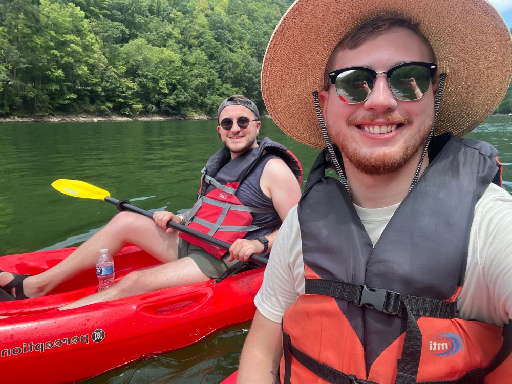Selfie of me and my husband while kayaking on a lake. We are smiling with sunglasses and hats on.