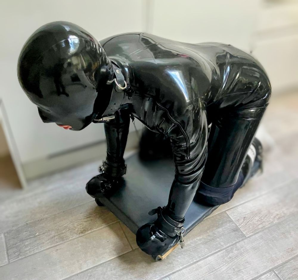 Rubber gimp kneeling on bondage board