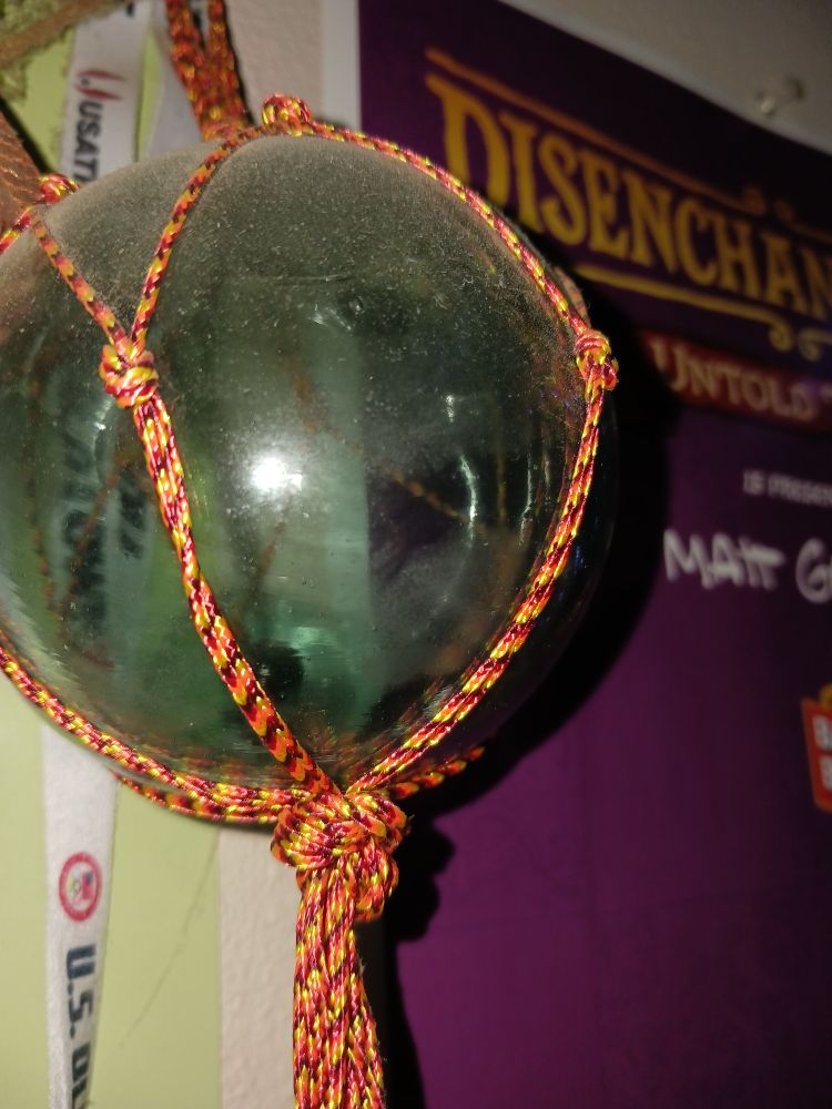 Antique Japanese glass float wrapped in orange string behind a purple poster