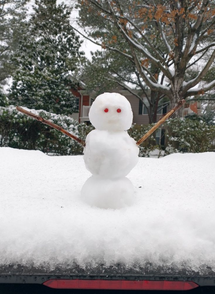 Small snow person with stick arms and red berry eyes