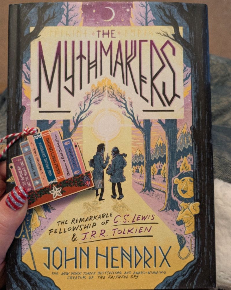 A photo of the book called The Mythmakers by John Hendrix and a wooden Christmas ornament of some Christmas themed books