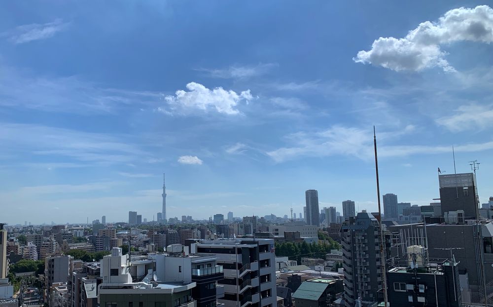Cityscape of Tokyo, blue skies, fluffy clouds.  Skytree visible in distance.