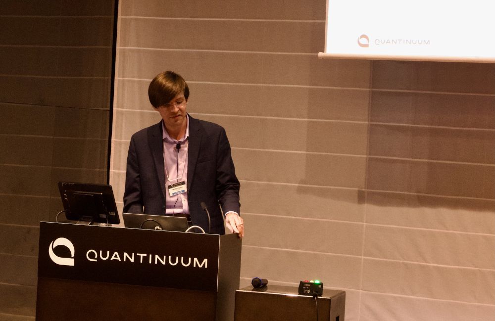 Nathan Lysne standing behind a podium.  The podium has "Quantinuum" written on it.