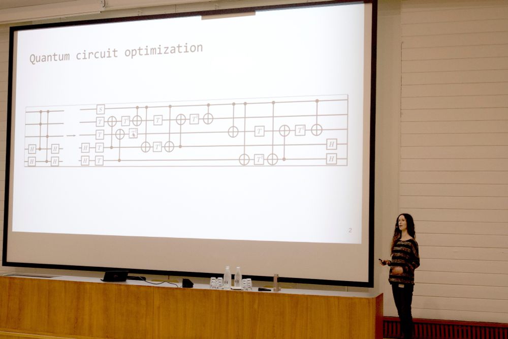 Olivia Di Matteo stands next to a giant screen showing a quantum circuit.