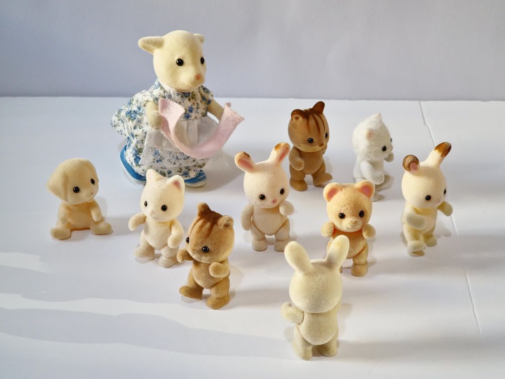 A Sylvanian adult goat, in a blue and white floral dress, chases a group of naked baby sylvanians brandishing a towel. She looks poised to capture a contemplative rabbit baby while the others of varying species scatter in every direction. One rabbit baby has its back to the camera with arms raised, as if trying to alert the other, unaware baby.