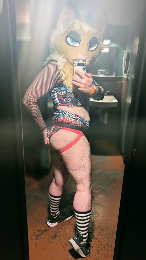 me in a colorful trippy matching top and bottom set, with fishnet features. I'm also wearing my fursuit, a pink jockstrap, and black and white striped socks. showing off my ass.