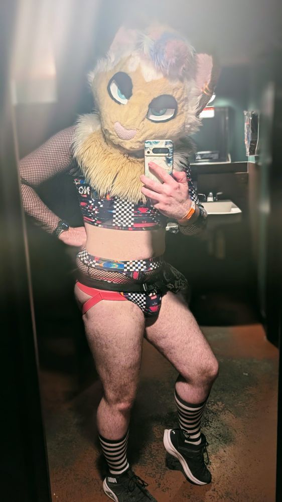 me in a colorful trippy matching top and bottom set, with fishnet features. I'm also wearing my fursuit, a pink jockstrap, and black and white striped socks. showing off my front.