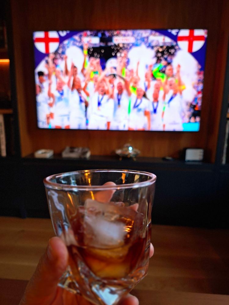Foto of glass of rum and ice and England v Brazil programme on the tv in the background 