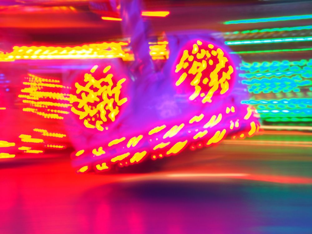Leuchtende Lichter eines Fahrgeschäfts auf einer Kirmes,durch die Bewegung verwischt 