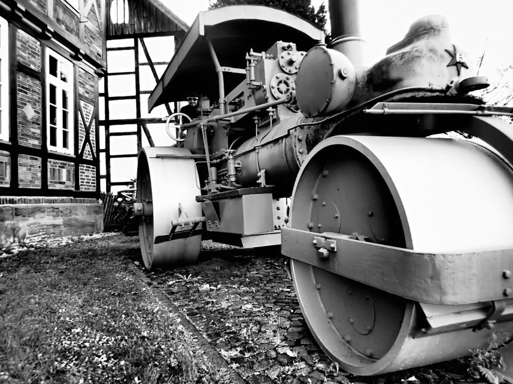 Eine Straßenwalze, angetrieben per Dampfmaschine, vor Fachwerkfassaden