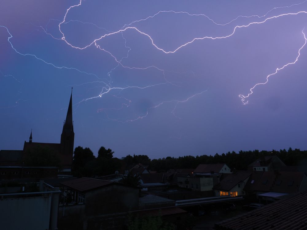 Linkd ein Kirchturm, am Himmel mehrere Blitze