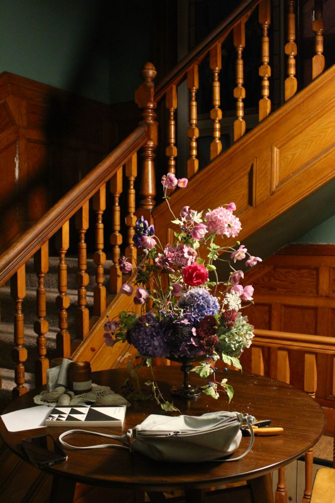 Some flowers in a vase on a small table in front of the staircase in my house (a sweet cheap old house I got!)