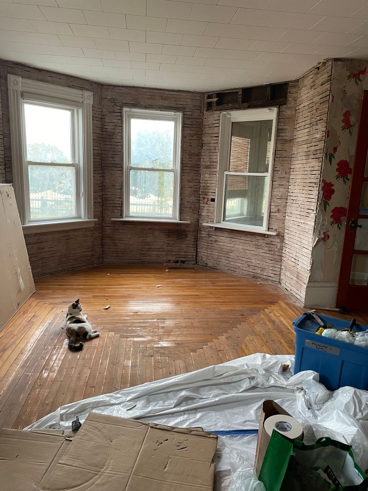 My living room shortly after possession - house was built in the 1870s, we remediated mold all around the three bay windows and ended up tearing out plaster along all the exterior walls. Floors are the original hardwood, in this photo they are in bad shape.