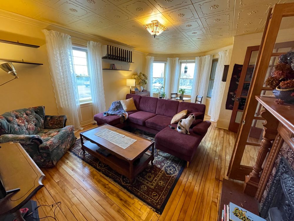 My living room, mostly finished. Floors are refinished original hardwood, walls are what I call "creamy mango" and ceilings are ornamental tiles in a soft peachy gold. Curtains are creamy lace, sofa is u-shaped and wine red corduroy, and there's a tealish floral velour armchair. Ceiling light is tiffany-style, rug is dark Persian-style, tables are all thrifted antiques.