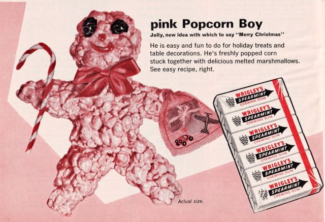An ad from Woman’s Day Magazine (Dec 1964), including a recipe for Pink Popcorn Boy, a treat like rice crispie squares but with popcorn and red-dyed marshmallows. He is pink and naked and his whole body looks like pink guts. He has shriveled brown eyes (raisins), a red dot nose and a red smile, and a big red bow around is neck. He is holding a candy cane and a bag of tiny toys. 