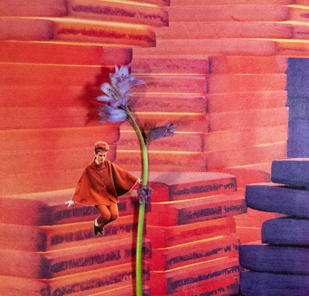 Red-haired woman dressed in 60’s attire is holding a purple flower. She is seated among thermal colored (red/orange, purple) blocks.  
