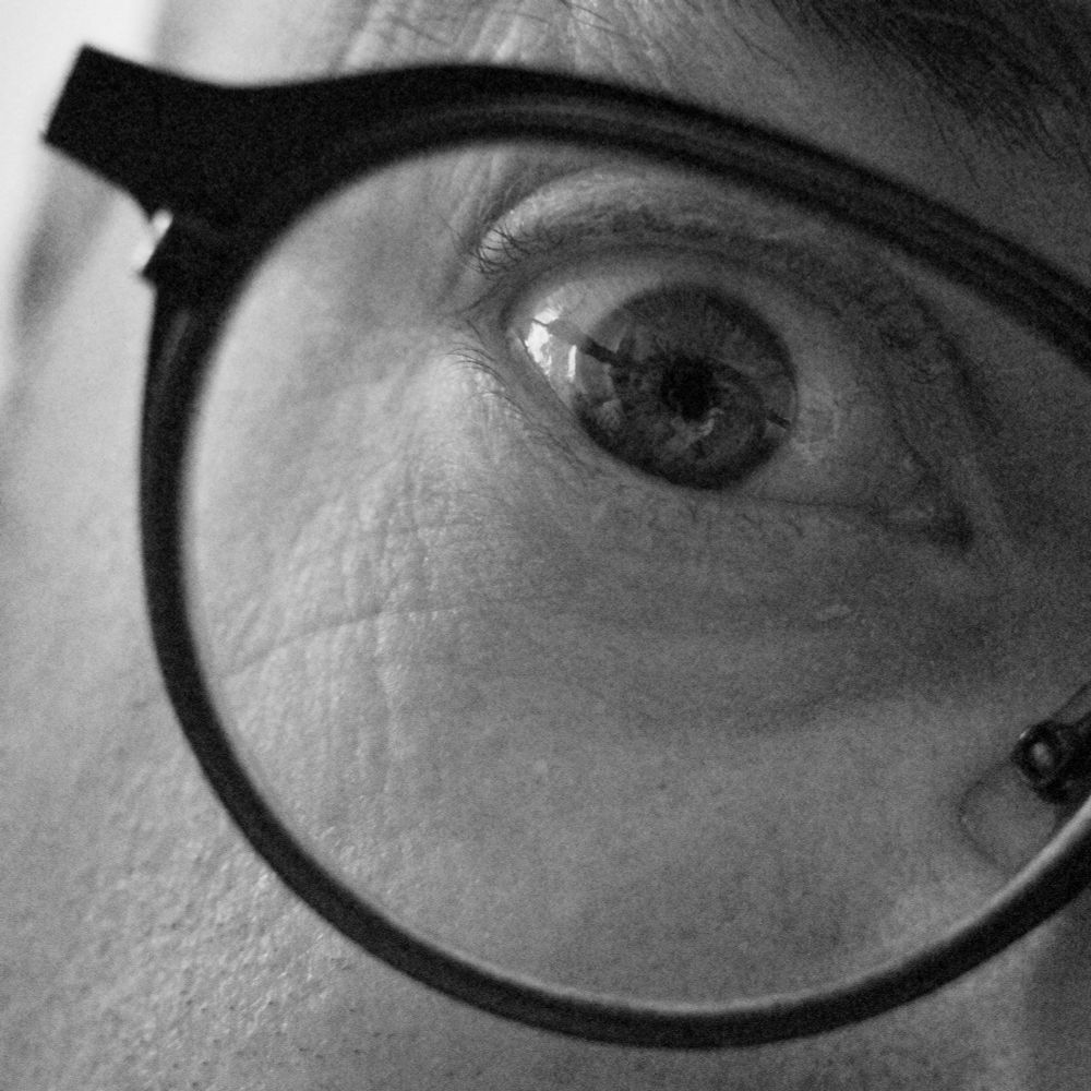 A black and white photo of a man's eye. He is wearing glasses. 
