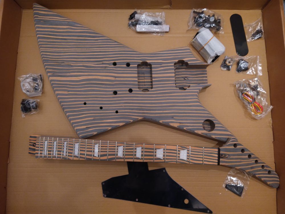 Guitar body, neck, electronics, and hardware spread over a cardboard box