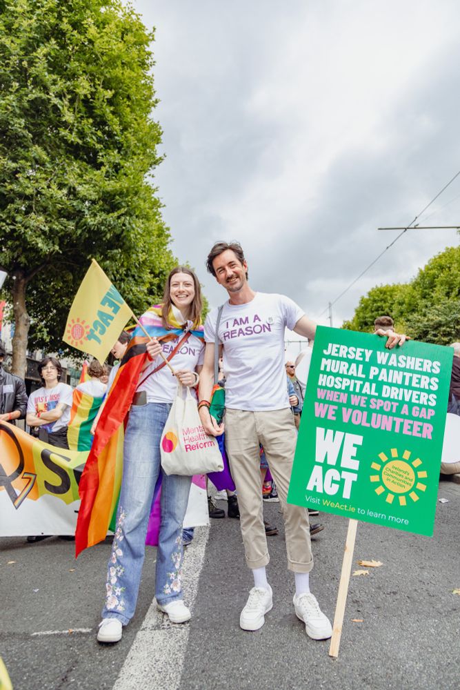 People at Dublin Pride, dressed colourfully with We Act placards and flags. 