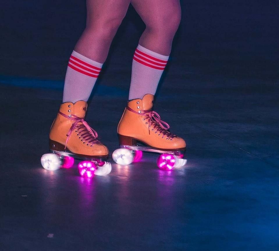 A pair of orange roller skates with white and pink light up wheels. 